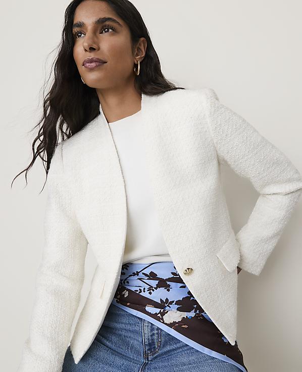 A woman in a white textured blazer and blue jeans is captured against a plain, light background.