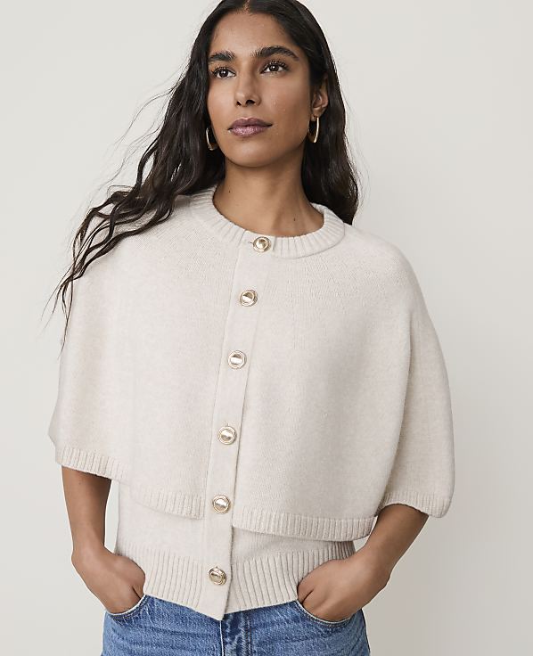 A woman in a cream-colored cardigan and jeans stands against a plain white background.