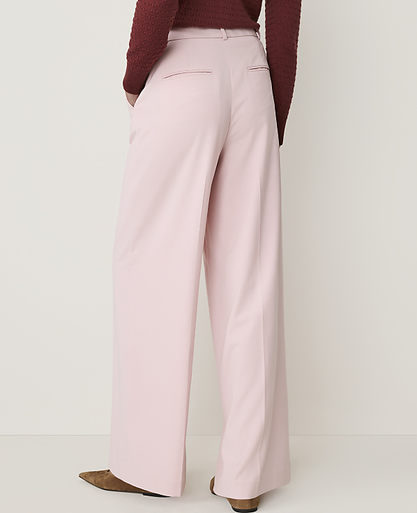 A person wearing pink wide-leg pants and a maroon sweater stands against a plain white background.