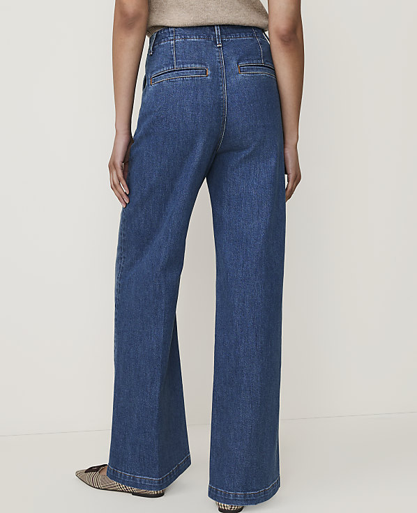 A person wearing wide-leg denim jeans and patterned flats stands against a plain, light-colored background.