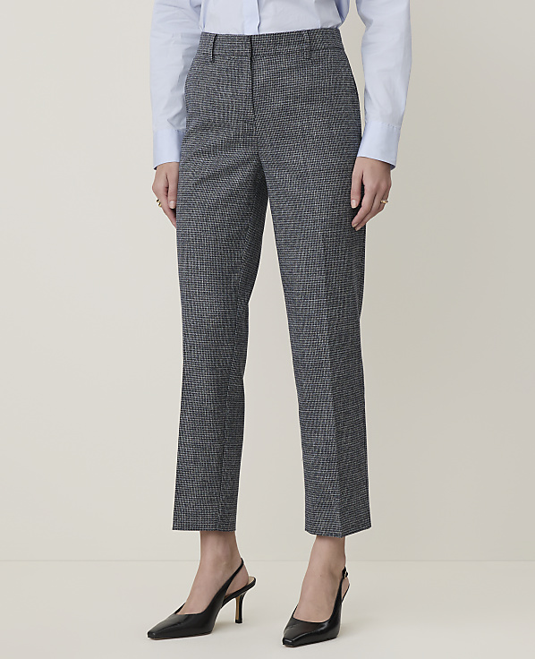 A person stands in a light gray room wearing a blue shirt and patterned gray pants with black heels.