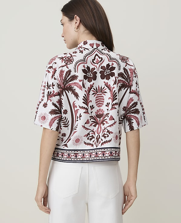 A woman in a patterned shirt stands against a plain background.