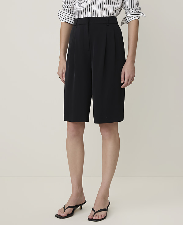 A person stands in black culottes and a striped shirt against a plain, light-colored background.