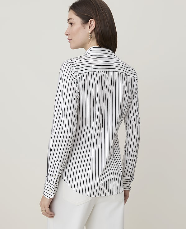 A woman in a striped shirt and white pants stands against a plain, light background.