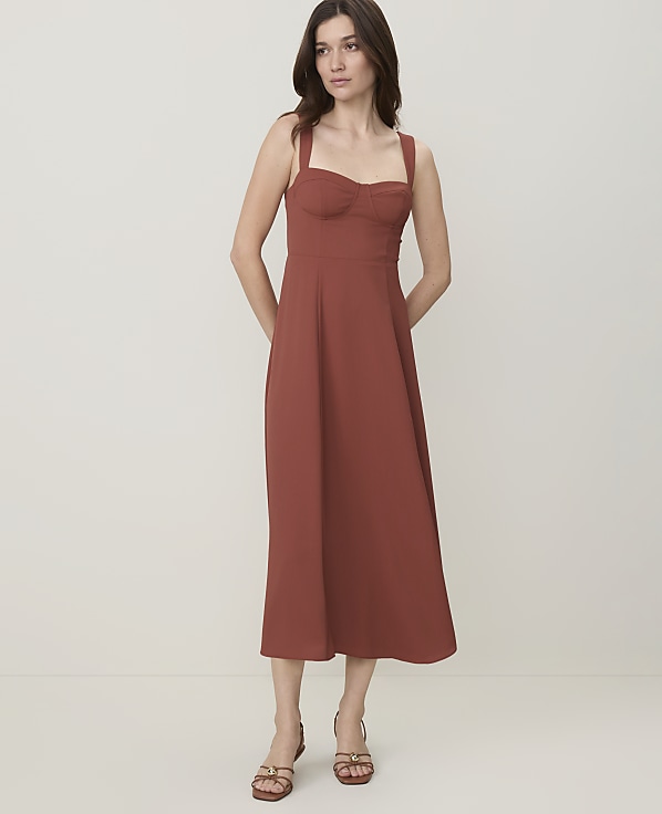 A woman in a rust-colored midi dress stands against a plain, light-colored background.