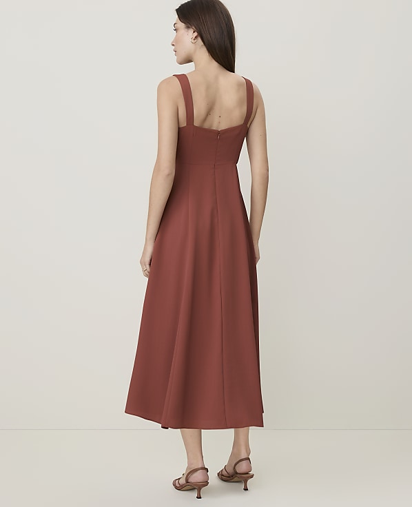 A woman in a rust-colored midi dress stands against a plain, light-colored background.