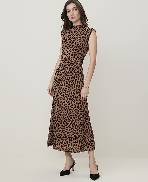 A woman in a leopard print dress stands against a plain, light-colored background.