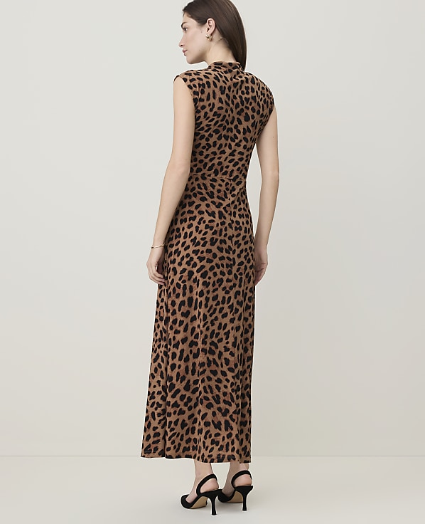 A woman in a leopard-print dress stands against a plain, light-colored background.