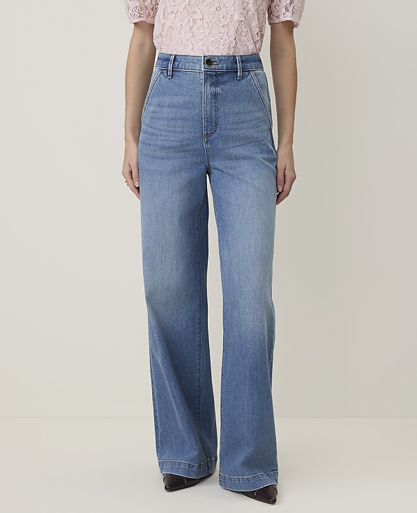 A person in a pink lace top and light blue wide-leg jeans stands against a plain cream background.