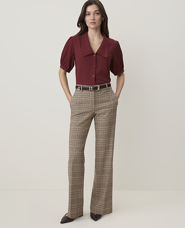 A woman in a maroon blouse and plaid pants stands against a plain, light-colored background.