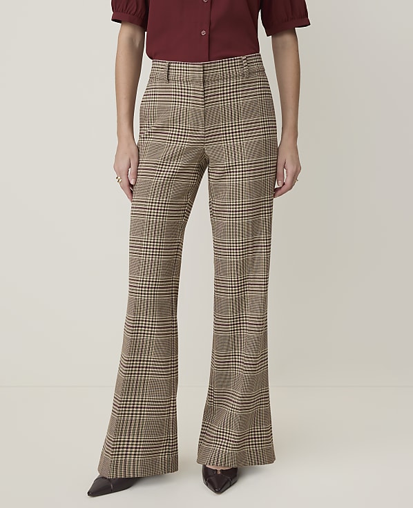 A person stands in flared plaid trousers and a maroon blouse against a plain, light-colored background.