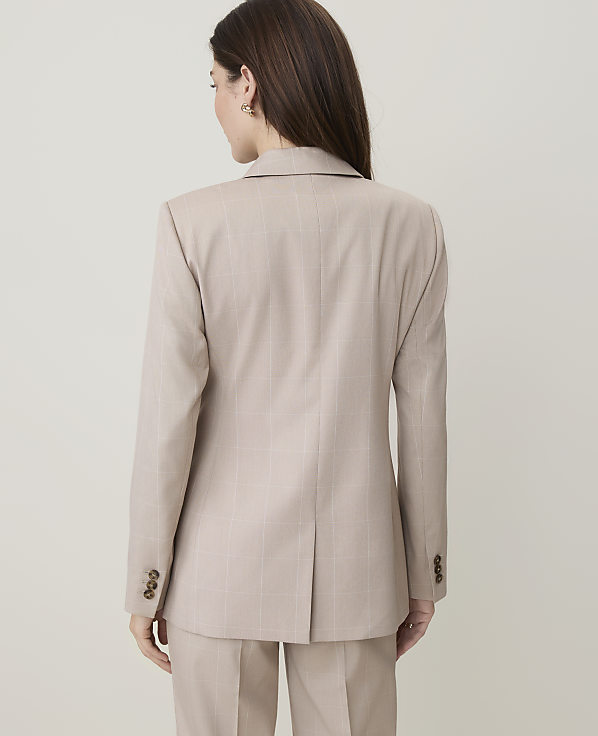 A woman in a beige plaid suit stands against a plain, light-colored background.