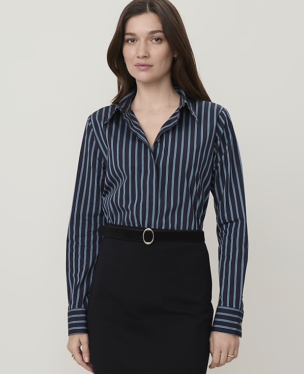 A woman in a striped blouse and black skirt stands against a plain background.