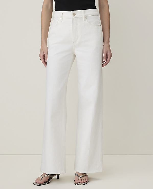 A person stands in white wide-leg jeans and patterned heels against a plain, light background.
