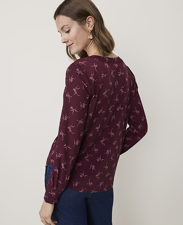 A woman in a maroon dinosaur-print blouse and dark jeans stands against a plain, light-colored background.