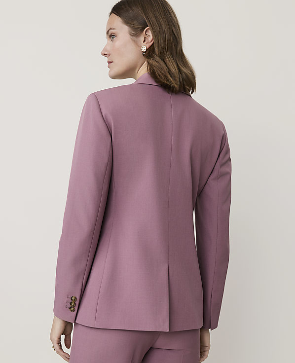 A woman in a mauve blazer and pants stands against a plain, light background.