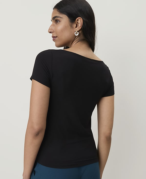 A woman in a black t-shirt and teal pants stands against a plain white background.