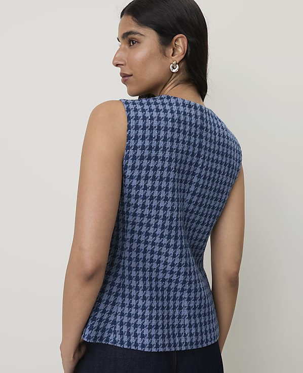 A woman in a blue houndstooth vest is shown from the back against a plain, light background.