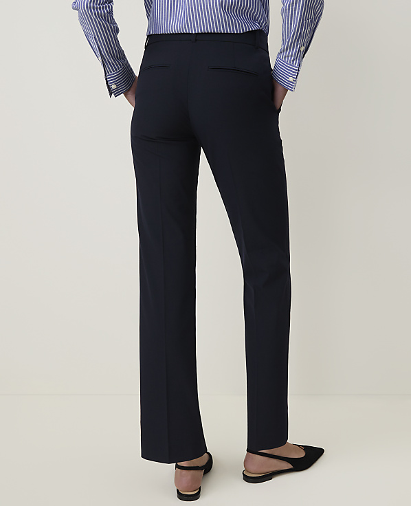 A person in a striped shirt and navy pants stands with hands in pockets, against a plain, light background.