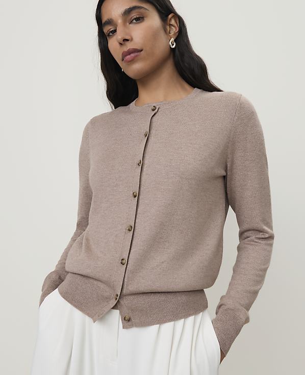 A woman in a beige cardigan stands against a plain, light background.