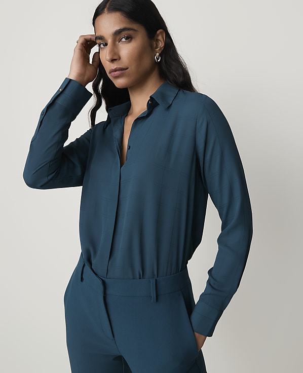 A woman in a teal blouse and matching pants stands against a plain gray background.