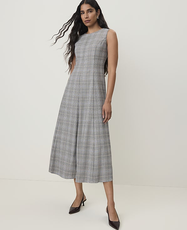 A woman in a plaid dress and heels stands against a plain, light background.