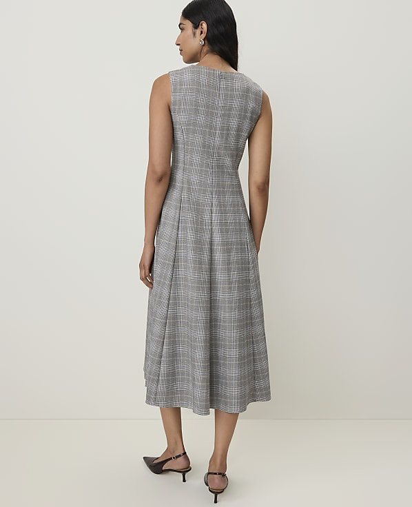 A woman in a grey plaid dress stands against a plain, light-colored background.