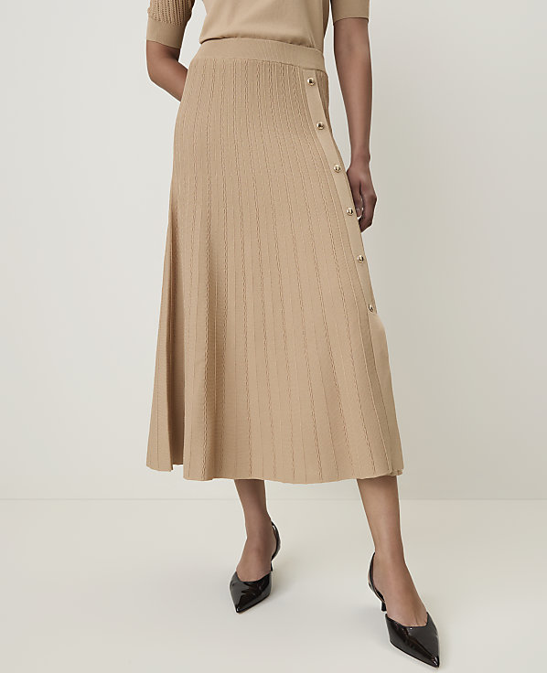A woman in a beige knit skirt and black heels stands against a plain white background.