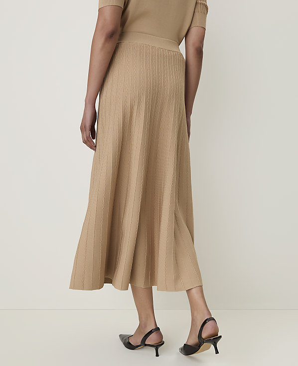 A woman in a beige knit skirt and top stands against a plain, light background.