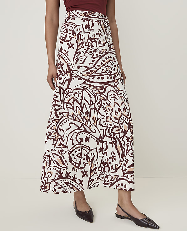 A woman in a patterned skirt and dark flats stands against a plain white background.