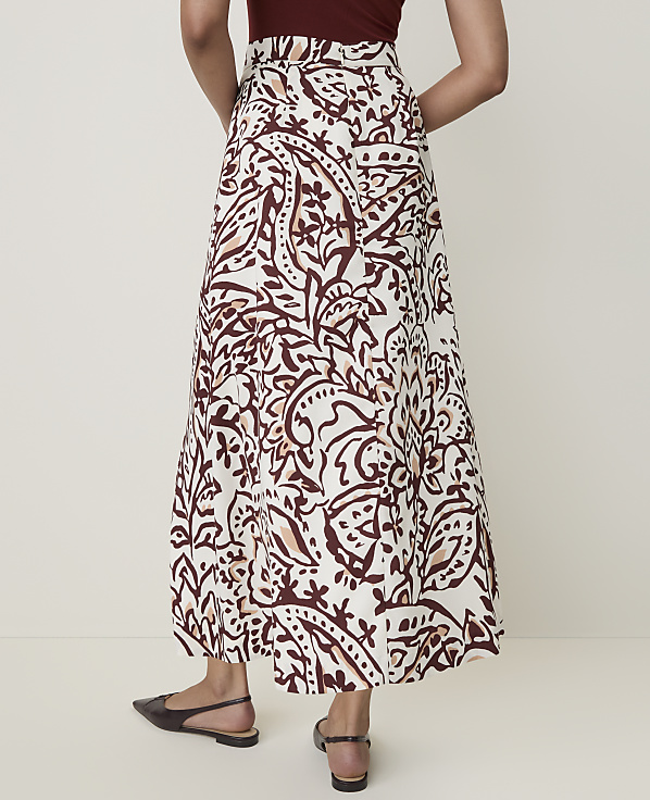 A woman in a patterned skirt and flat shoes stands against a plain background.