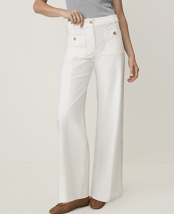 A person wearing white wide-leg pants and brown flats stands against a plain white background.