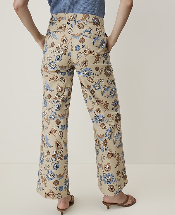 A person wearing beige floral-patterned pants and brown sandals stands against a plain white background.