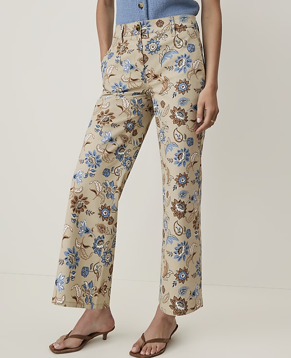 A person stands in the foreground wearing tan pants with a blue and brown floral pattern, against a plain, light-colored background.