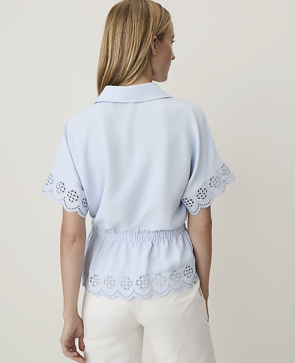 A woman in a light blue blouse with eyelet details stands against a plain, light background.