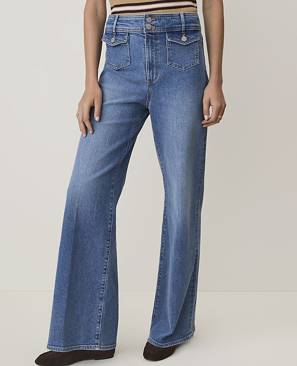 A person wearing high-waisted, flared denim jeans with large front pockets stands against a plain, light-colored background.