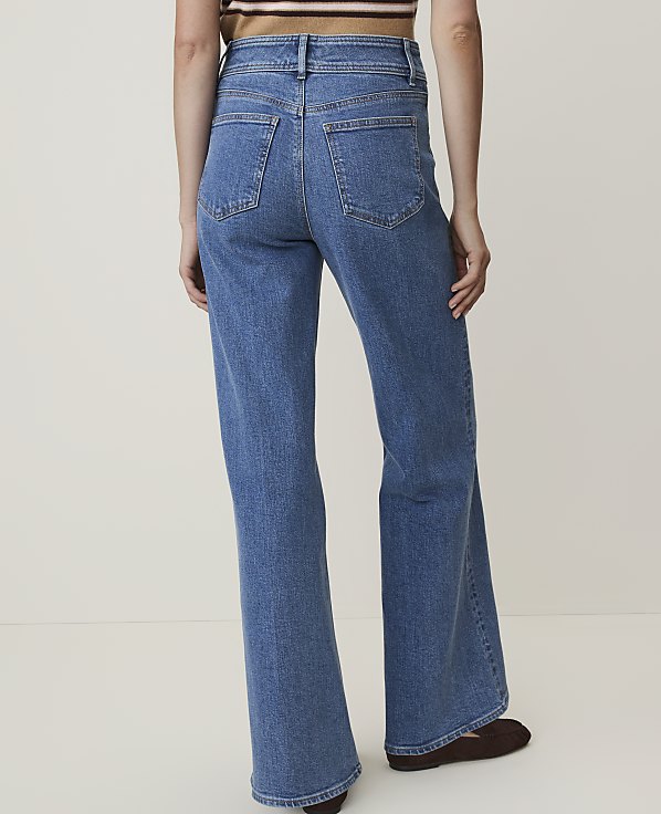 A person wearing wide-leg blue jeans stands against a plain, light-colored background.