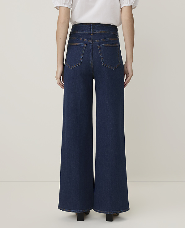 A person wearing dark wash wide-leg jeans stands against a plain, light-colored background.