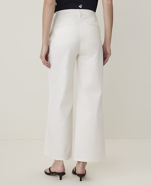 A person wearing white wide-leg pants and black sandals stands against a plain, light-colored background.