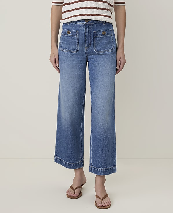 A person wearing wide-leg denim jeans and brown sandals stands against a plain white background.