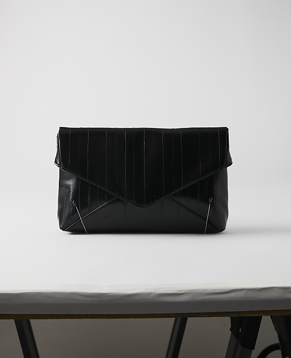 A black, textured envelope clutch rests on a white surface against a plain white background.
