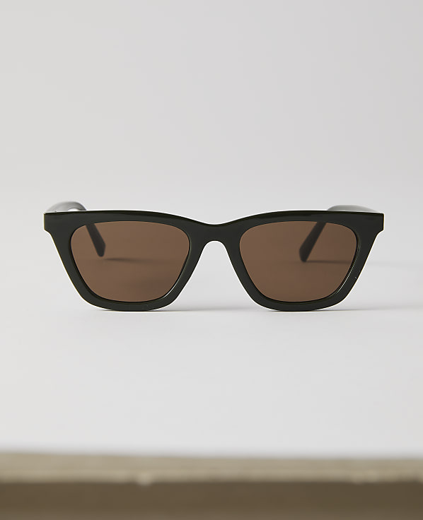 Black-rimmed sunglasses with brown lenses rest on a white surface against a plain white background.