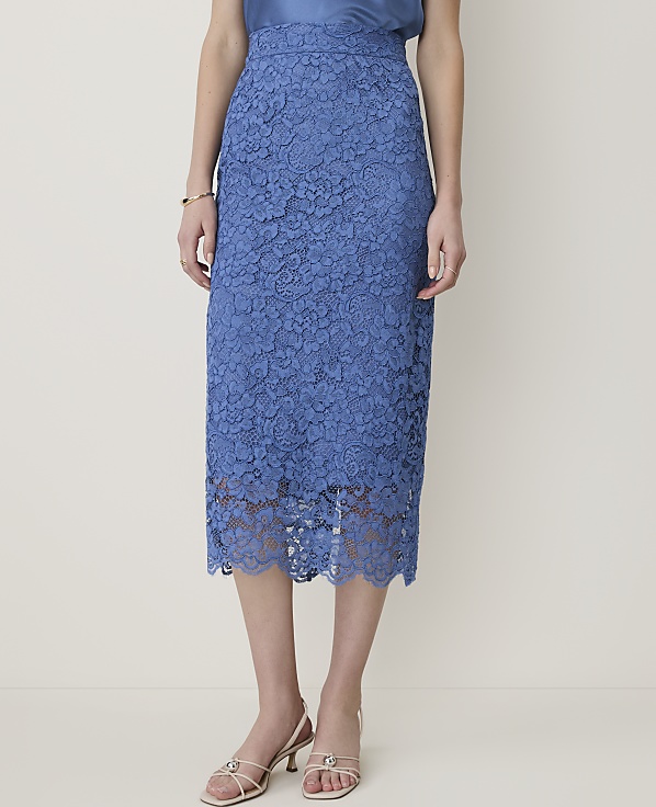 A woman in a blue lace skirt and white sandals stands against a plain, light-colored background.