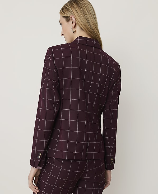 A woman in a burgundy plaid blazer and matching pants stands against a plain, light-colored background.