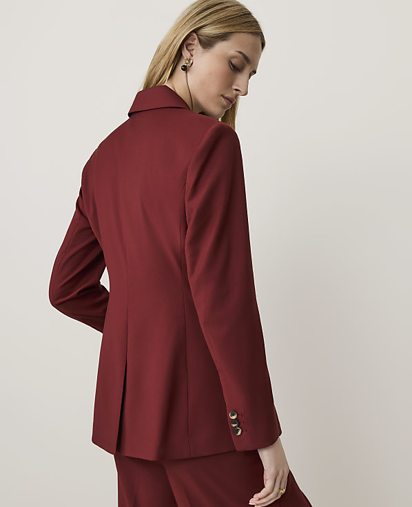 A woman in a maroon blazer and pants stands against a plain, light background.