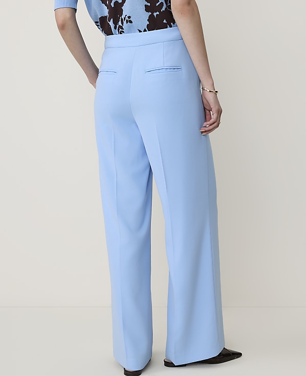 A person wearing light blue wide-leg trousers and a patterned top stands against a plain, light-colored background.