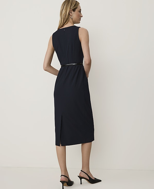 A woman in a navy dress and black heels stands against a plain white background.