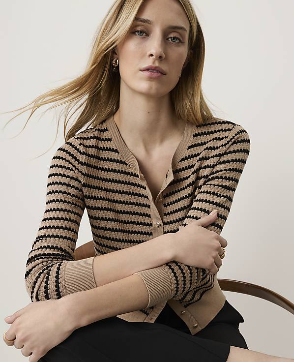 A woman with blonde hair and a striped cardigan sits in front of a plain, light-colored background.