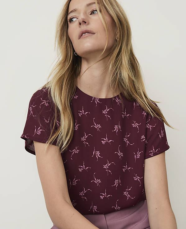 A woman with blonde hair wearing a maroon floral top is shown against a plain background.