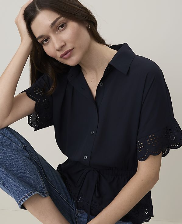 A woman in a navy blue shirt and jeans poses against a plain background.